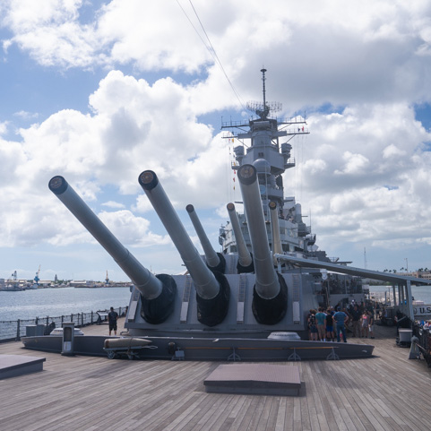 USS Missouri deck View from the wooden deck of the USS Missouri battleship, looking up at three massive 16-inch gun barrels and the main superstructure against a cloudy sky